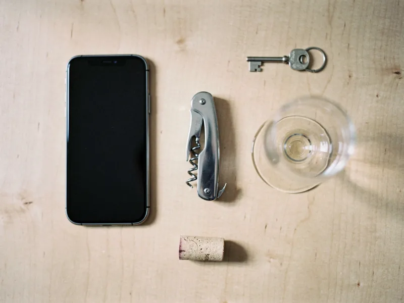 Smartphone mit dunklem Bildschirm auf einem Holzbrett neben einem Korkenzieher und einem Weinkorken